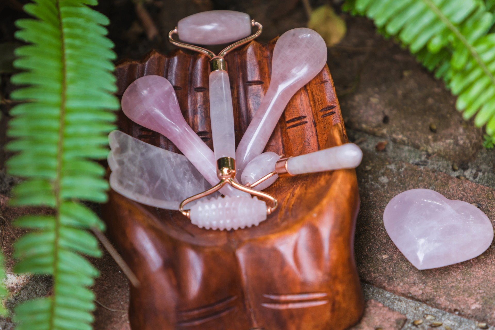 Rose quartz facial rollers and gua sha tools on a carved wooden stand