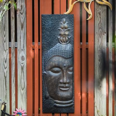 Bronze Buddha wall panel against the bungalow's orange cedar fence